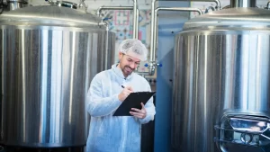 Profissional da indústria realizando inspeção técnica entre tanques de aço inox em ambiente de caldeiraria industrial