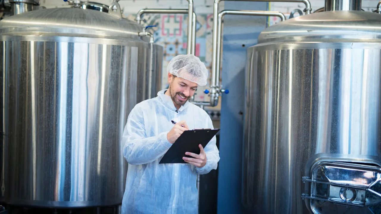 Profissional da indústria realizando inspeção técnica entre tanques de aço inox em ambiente de caldeiraria industrial